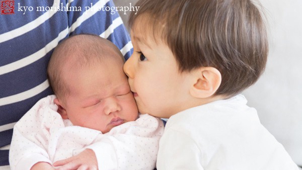 Toddler boy kissing newborn baby, photographed by NYC family photographer Kyo Morishima