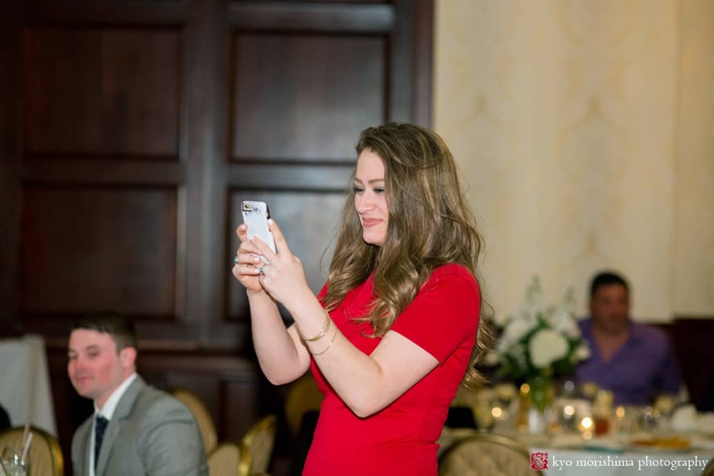 Guest wearing red dress takes an iphone photo during Nassau Inn wedding reception, photographed by Kyo Morishima