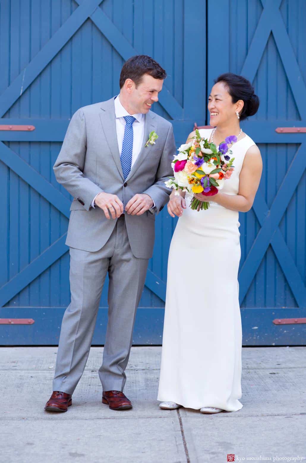 Portrait of bride and groom laughing in front of blue door; bride holds bouquet by Molly Oliver Flowers. photographed by Kyo Morishima