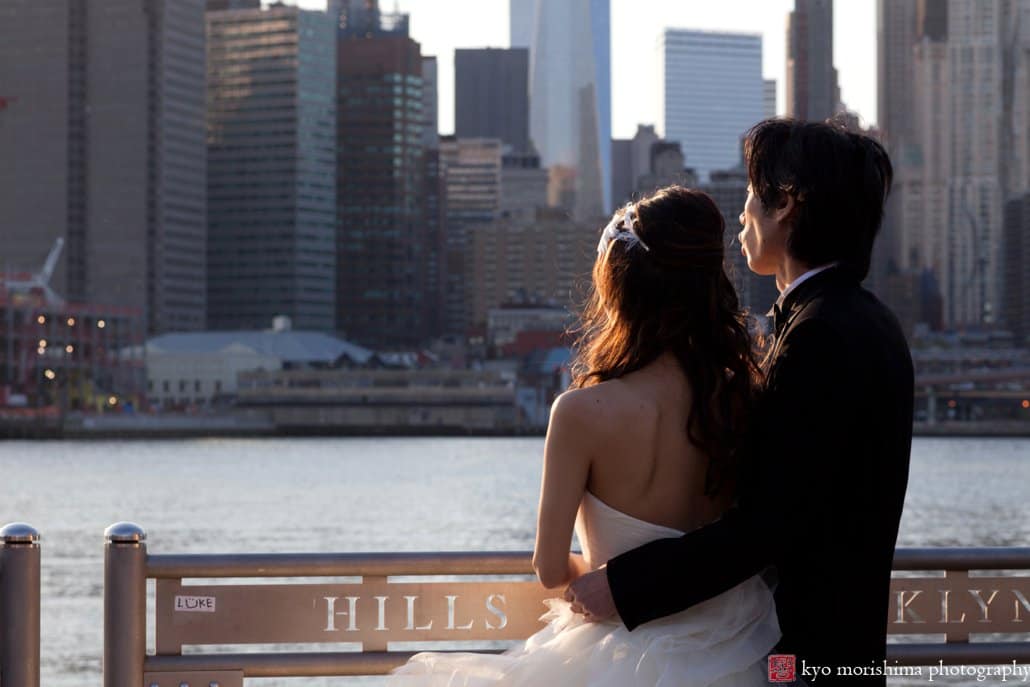 Japanese couple at dusk on their NYC wedding photo tour gaze at Manhattan skyline across the East River, photographed by Kyo Morishima