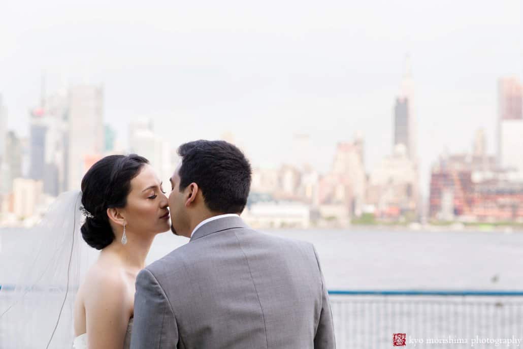 Bride and groom kiss with view of Manhattan in the background, at Weehawken Waterfront Park, photographed by NJ wedding photographer Kyo Morishima