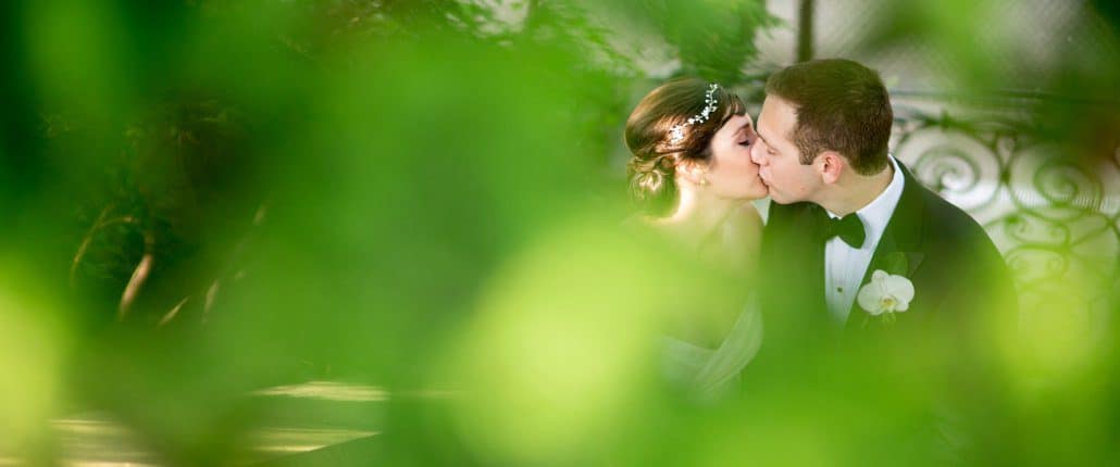 A glimpse of bride and groom kissing through greenery at Jasna Polana, photographed by Princeton wedding photographer Kyo Morishima