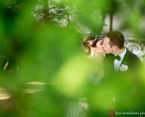 A glimpse of bride and groom kissing through greenery at Jasna Polana, photographed by Princeton wedding photographer Kyo Morishima