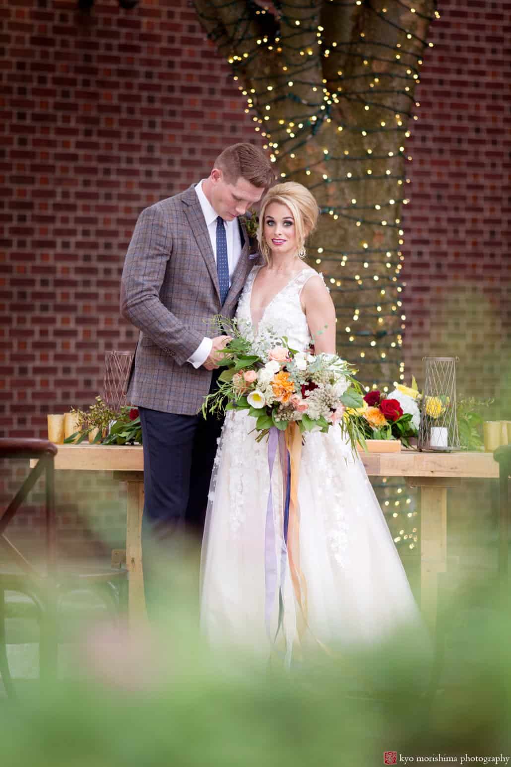 Bride wearing Ariane wedding gown from BHLDN with groom in front of West Elm table on back patio at Nassau Inn 