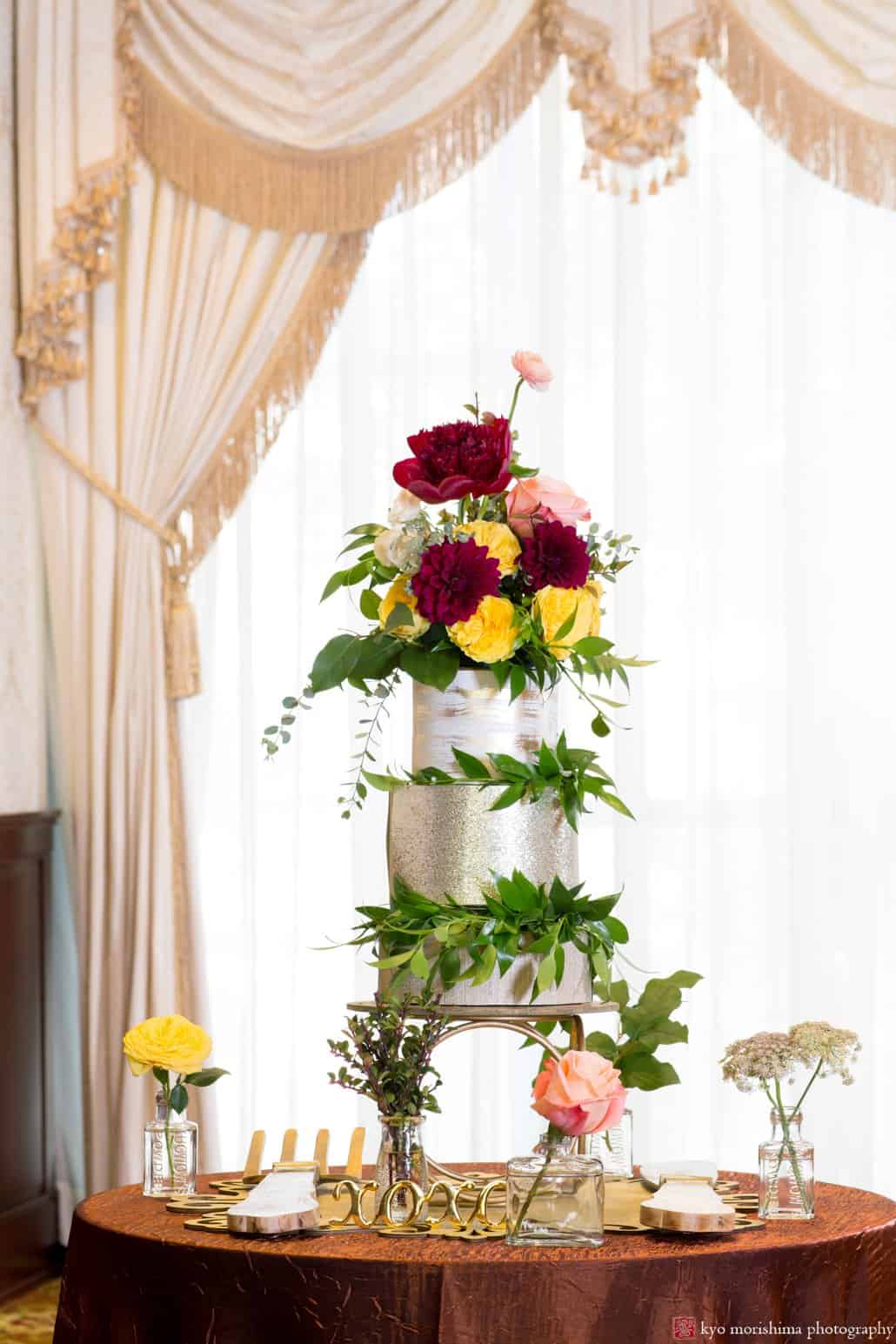 Gold and silver frosted wedding cake with maroon and gold flower decorations by Kristin Rockhill of Details of I Do, photographed in the Nassau Inn ballroom by Kyo Morishima.