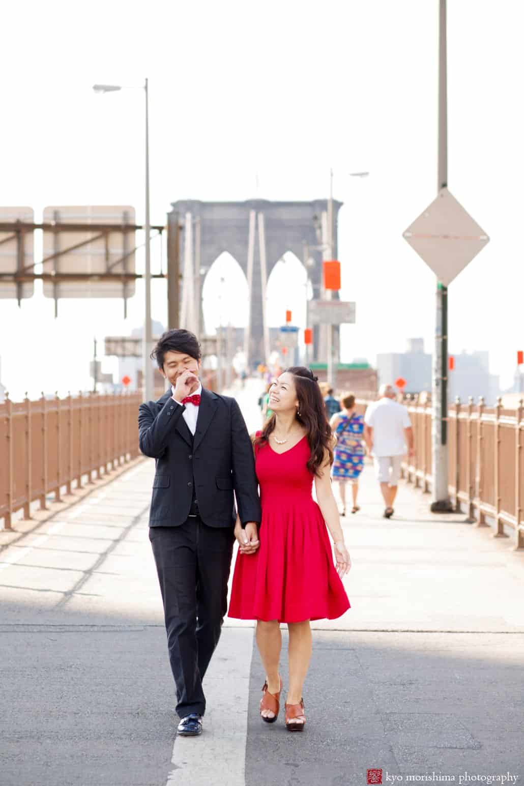 Japanese couple laughing as they walk along the Brooklyn Bridge; engagement photo photographed by Kyo Morishima