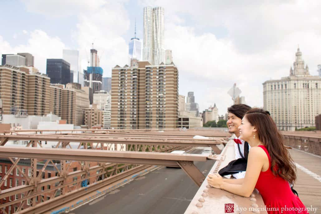Japanese couple gazes at Brooklyn skyline from Brooklyn Bridge during their engagement photo session photographed by Kyo Morishima