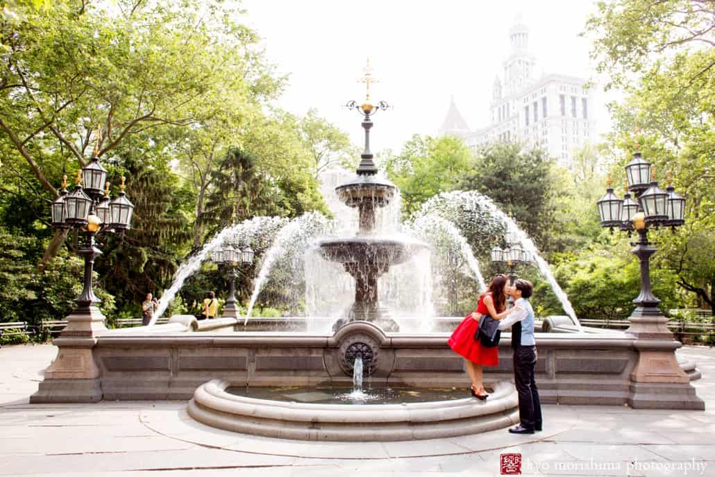 Japanese engagement photo in NYC: woman in red dress kisses man as they stand next to fountain, photographed by Kyo Morishima