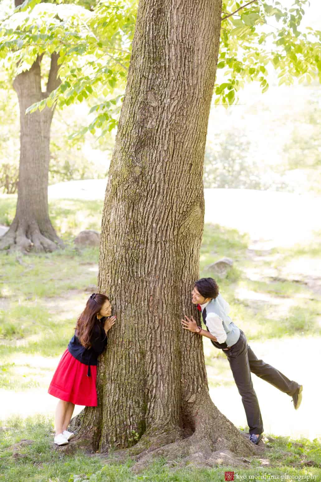 Japanese couple peek at each other around trunk of large oak tree in Central Park, photographed by Kyo Morishima