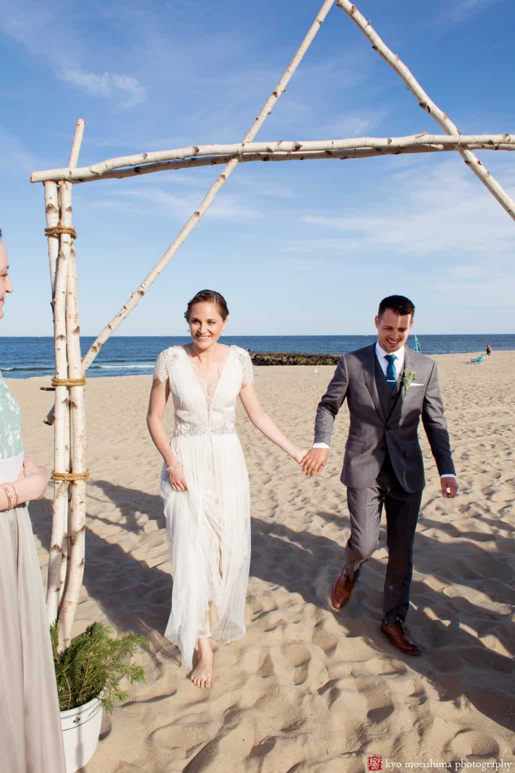 Bride and groom step under handmade arch during Asbury Park beach wedding ceremony, photographed by Kyo Morishima