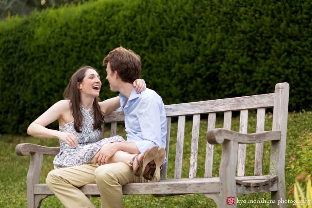 Couple sits on a bench and laughs during Prospect Gardens Princeton engagement session photographed by Kyo Morishima