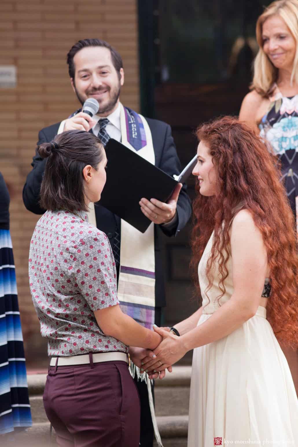 Bride and partner hold hands as Rabbi Eli Freedman from Congregation Rodeph Shalom concludes the wedding ceremony, photographed by Kyo Morishima