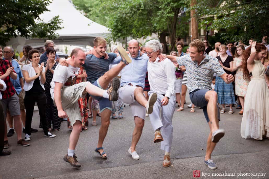 Male wedding guests line dance during West Philadelphia block party wedding photographed by Kyo Morishima