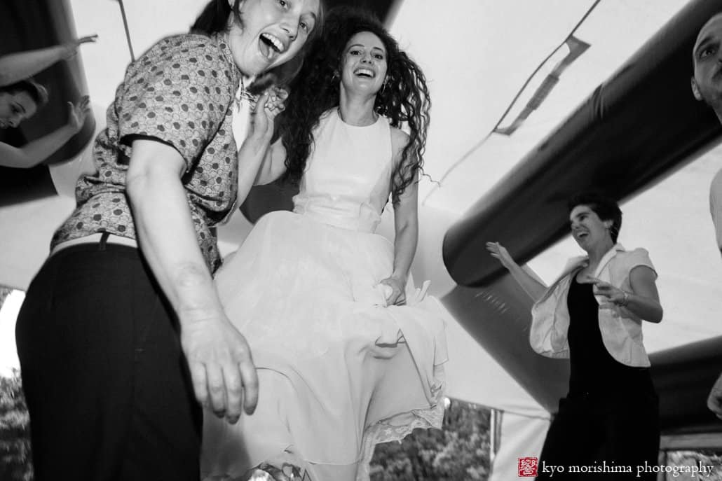 Bride and partner grin at camera while bouncing in the bouncy castle at block party wedding in West Philadelphia, photographed by Kyo Morishima