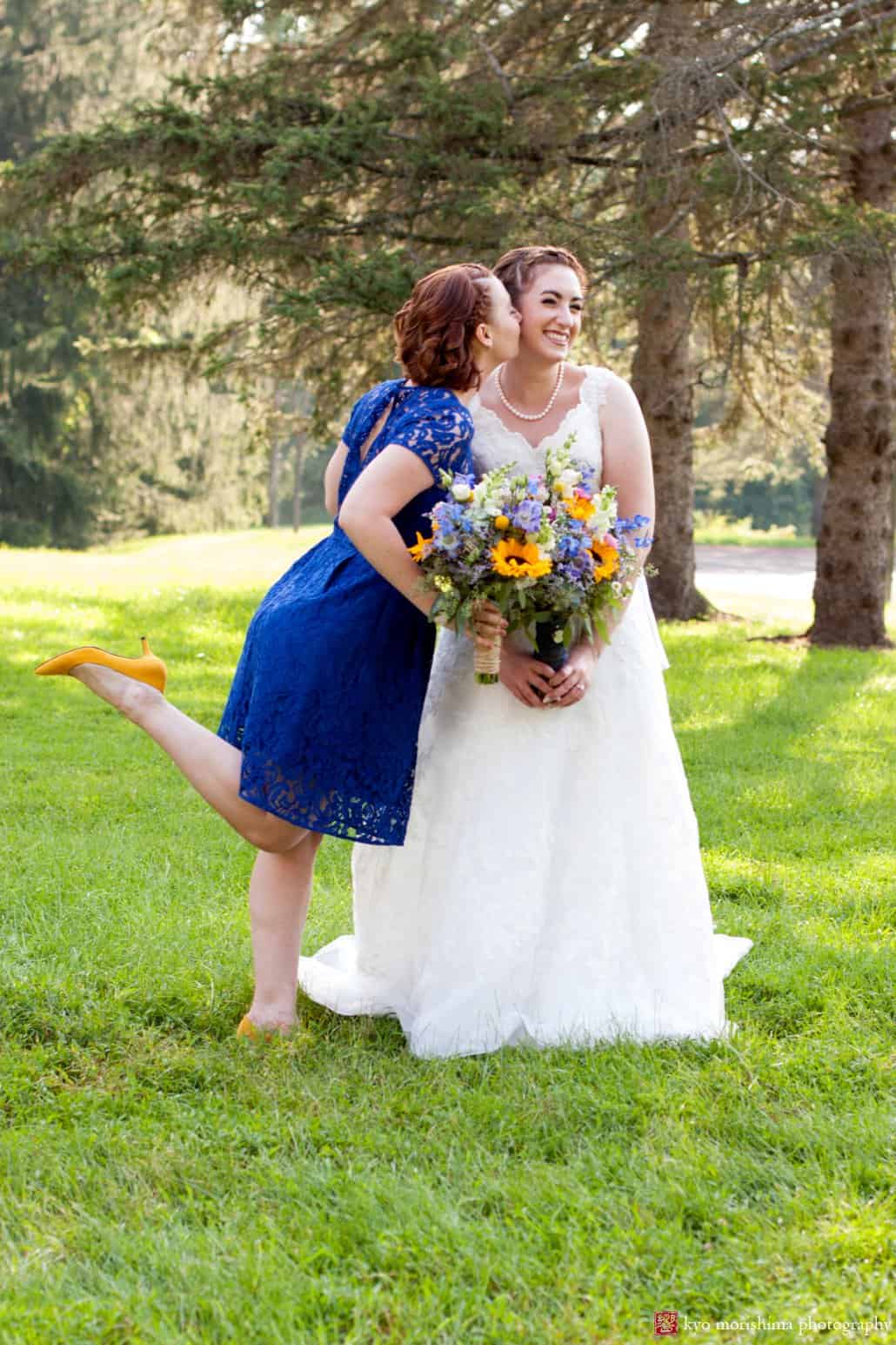 Maid of honor wearing royal blue bridemaid dress with yellow heels gives bride a kiss at Perona Farms wedding, photographed by Kyo Morishima