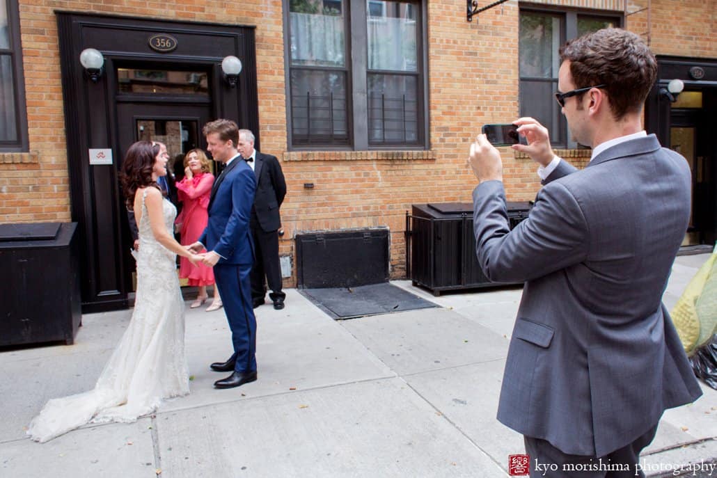 Groomsman photographs bride and groom first look on a Cobble Hill street, photographed by Brooklyn wedding photographer Kyo Morishima