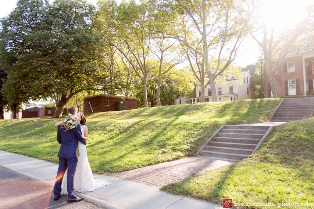 Bride and groom embrace as sun sets behind Governors Island mansion, photographed by Kyo Morishima