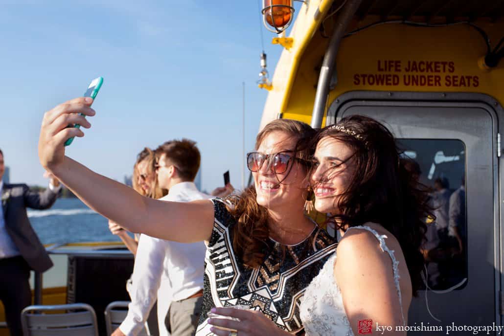 Bride and friend snap a selfie on board a NYC water taxi after Governors Island wedding, photographed by Kyo Morishima