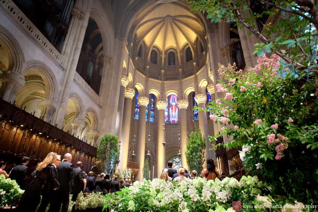 A glimpse of St. John the Divine wedding chapel decorated with trees and flowering shrubs, as wedding begins