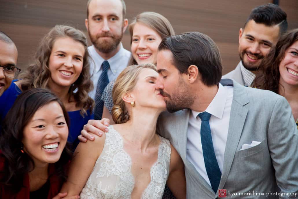 Bride and groom kiss while surrounded by friends as cocktail hour ends, photographed by Green Building wedding photographer Kyo Morishima