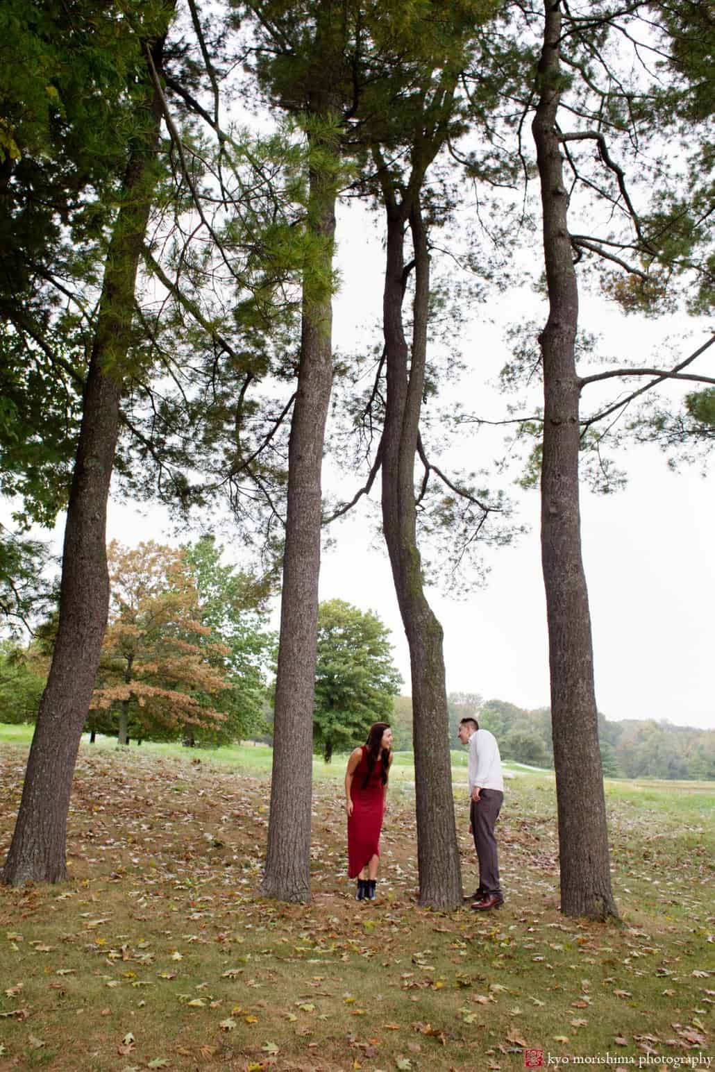 Couple peek at each other in a stand of pine trees at TPC Jasna Polana in Princeton, photographed by NJ wedding photographer Kyo Morishima