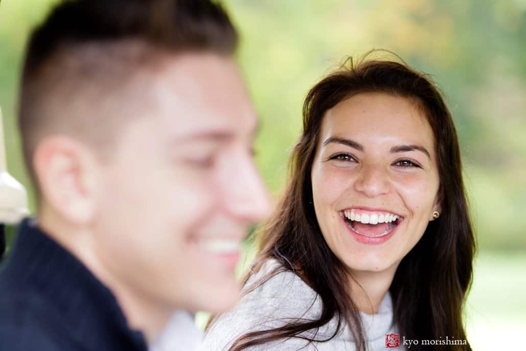 Creative engagement photo with woman laughing while fiancé smiles in foreground