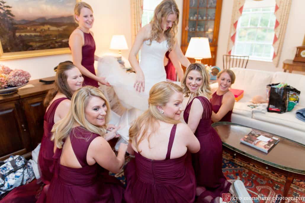 Bridesmaids glance back at ringbearer and smile as they help bride get dressed in Pronovias wedding gown