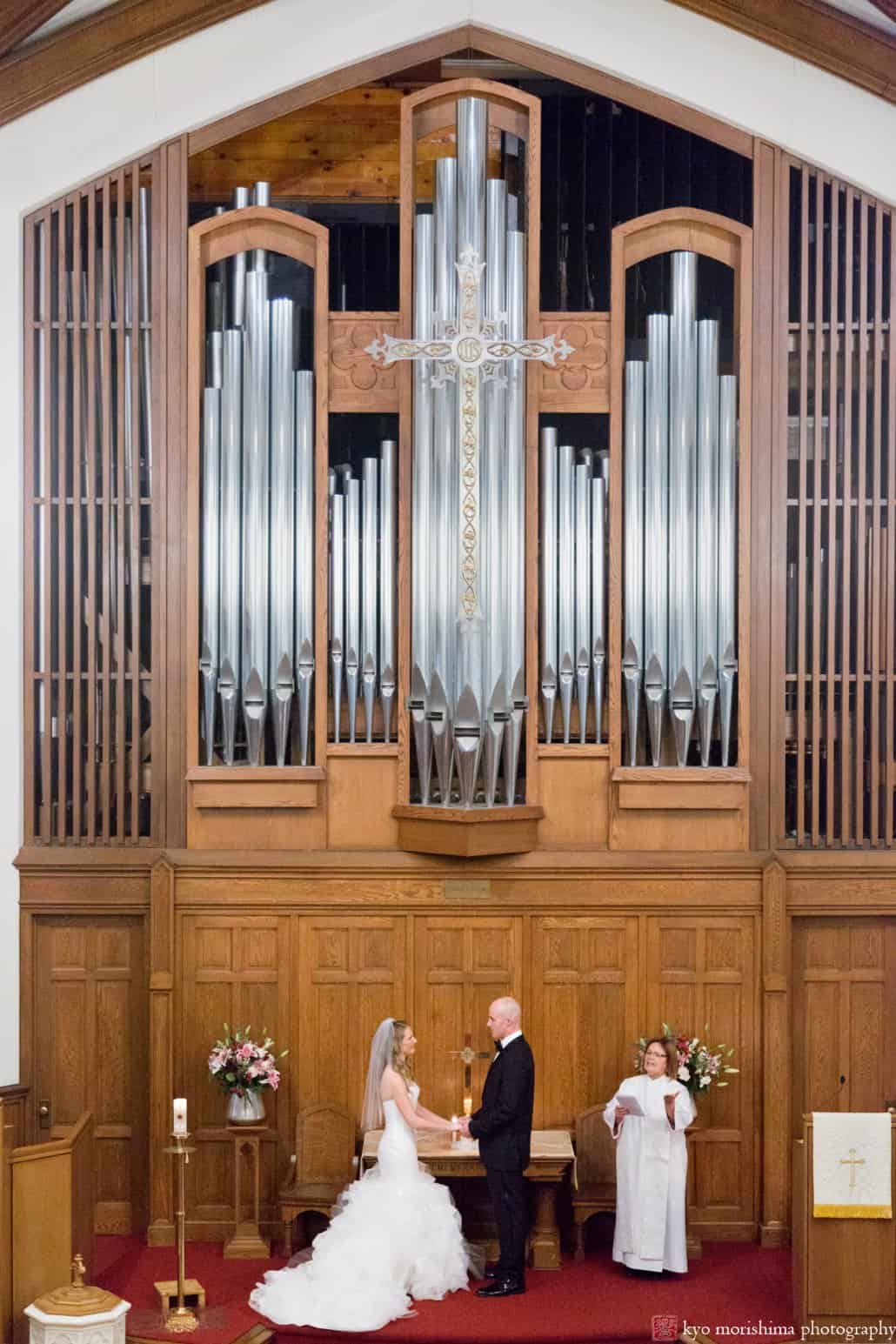 A wide view of bride and groom at the altar framed by organ pipes, photographed by Princeton United Methodist Church wedding photographer Kyo Morishima