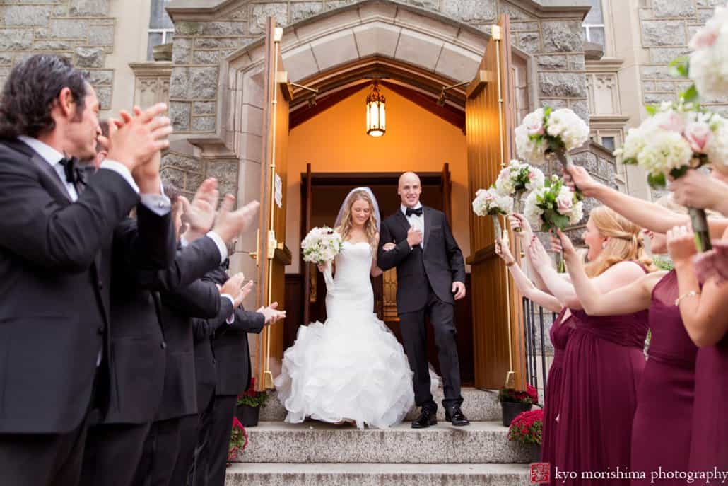 Bride and groom emerge happily from Princeton United Methodist Church wedding with bridesmaids and groomsmen clapping