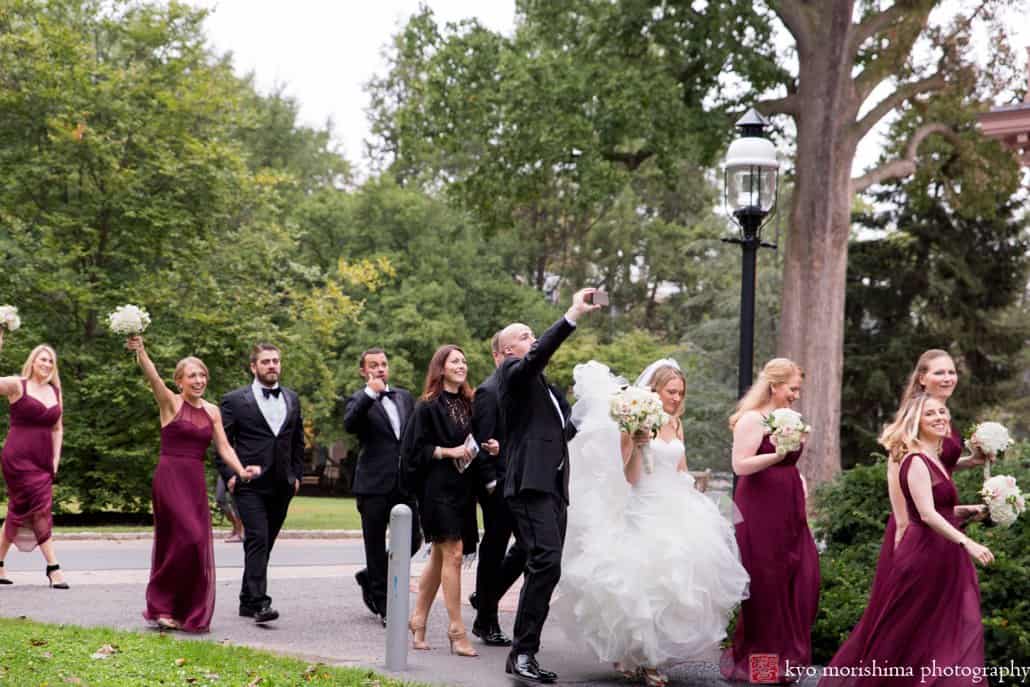 Groom takes a selfie as wedding party walks to wedding portrait location on Princeton University campus