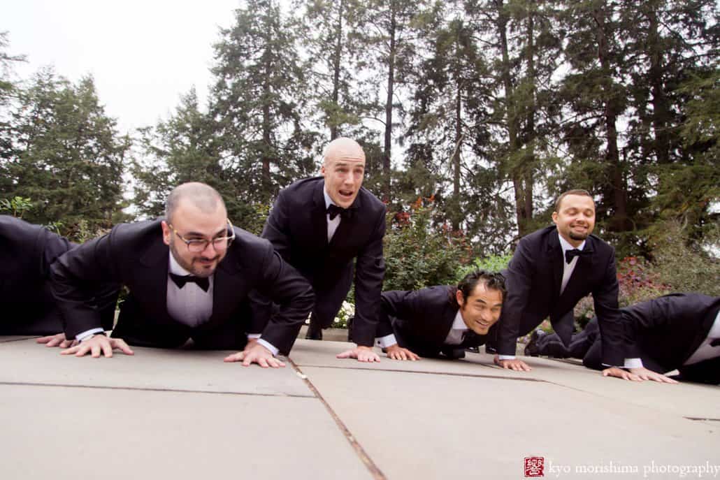 Groom rises above groomsmen while doing push-ups during wedding portrait session at Prospect Gardens