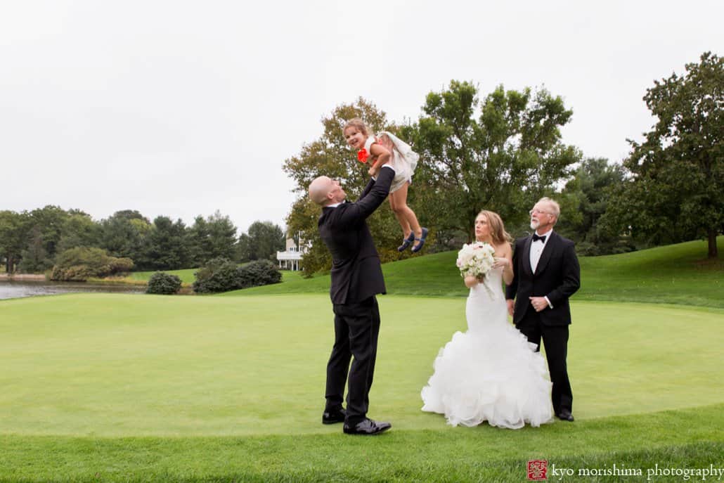 Groom lifts flower girl during family portrait session on the golf course at Cherry Valley Country Club wedding