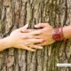 A couple clasp hands around a big oak tree trunk; the woman wears a vibrant gel manicure with a different finish on each fingernail.