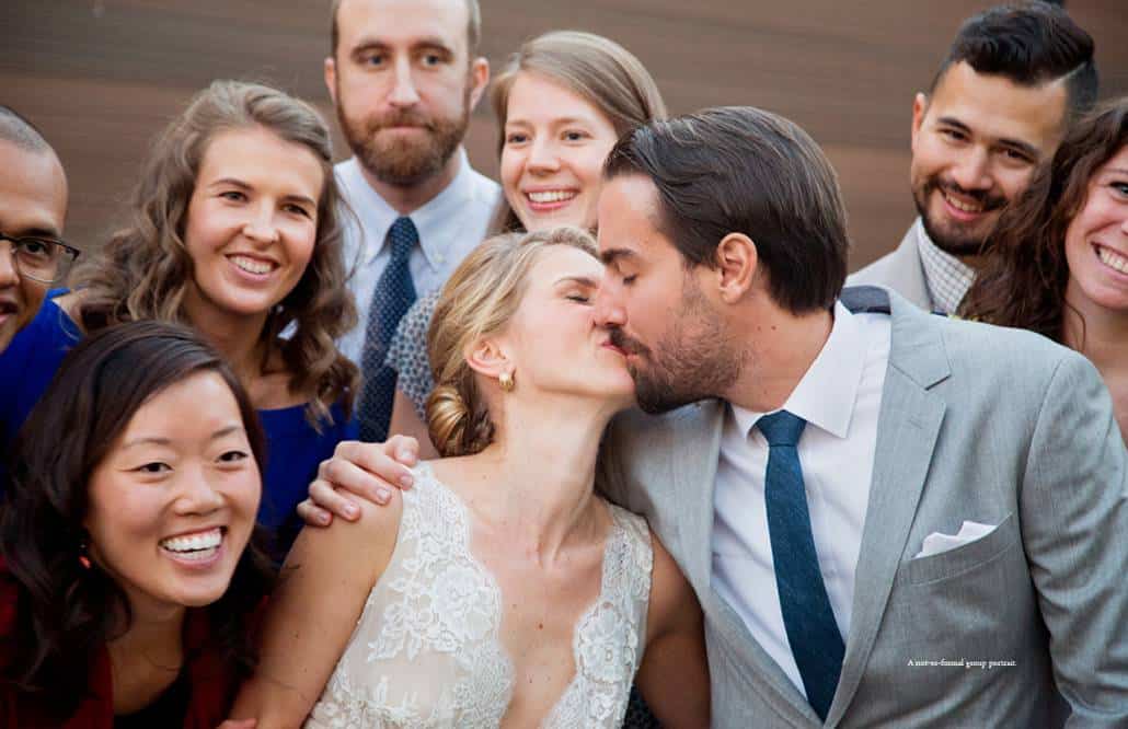 A very informal group portrait with the bride and groom kissing and surrounded by their friends at a Green Building wedding in Brooklyn