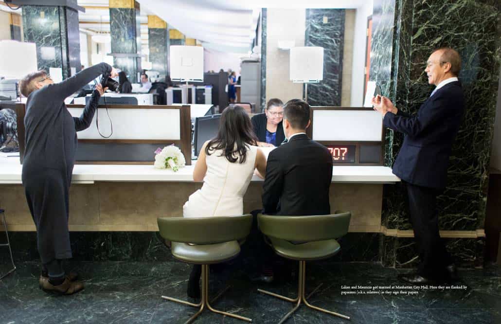 Manhattan City Hall wedding photographer: a couple signs their documents as relatives look on and photograph them