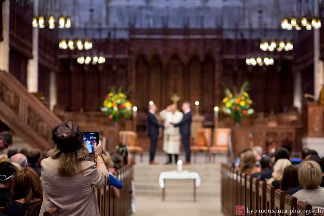 A guest photographs wedding ceremony at altar of Princeton University chapel