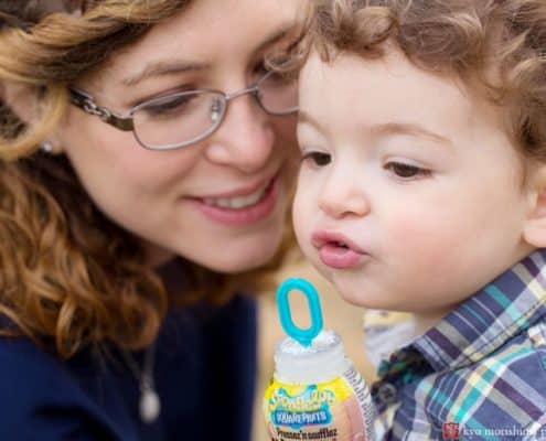 Candid family photographer central New Jersey: child blows bubbles with mom