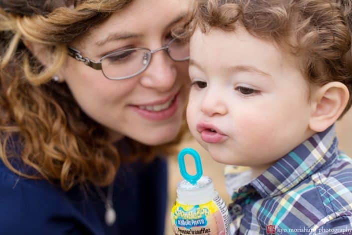 Candid family photographer central New Jersey: child blows bubbles with mom