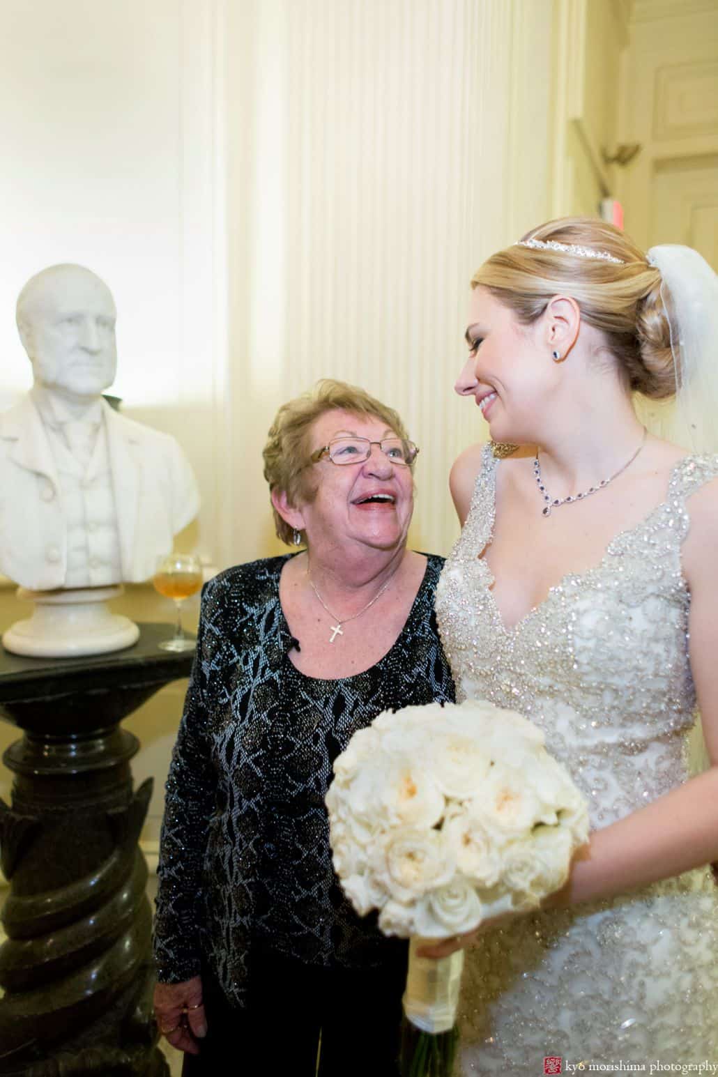 Bride wearing Allure Couture wedding dress smiles back at her Grandmother while holding a bouquet of white roses by Fleur Du Mois. Wedding photography by Kyo Morishima.