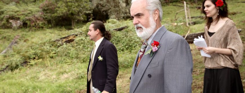 Father of the groom and two guests wait for bride on a mountaintop in San Gerardo de Dota for Costa Rican destination wedding. Girl with red rose in her hair, grey suit, red and pink rose boutonnnieres, Talamanca cloud forest background.