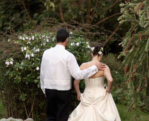 Bride and groom walk into Talamanca cloud forest, groom's hand on bride's shoulder, back laced corset wedding dress, cactus, succulents, rhododendron, flowers in bride's hair. Destination wedding photographer.