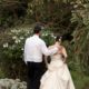 Bride and groom walk into Talamanca cloud forest, groom's hand on bride's shoulder, back laced corset wedding dress, cactus, succulents, rhododendron, flowers in bride's hair. Destination wedding photographer.
