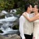 Bride and groom kiss in front of waterfall in Talamanca cloud forest, Costa Rica. Ivory satin wedding dress with white embroidered vines, taupe groom's vest and tie, flowers in brides hair, destination wedding photographer.