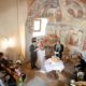 Bride and groom read together in tiny Romanesque church in Swiss Alps during European destination wedding ceremony. Domed alcove with painted mural.