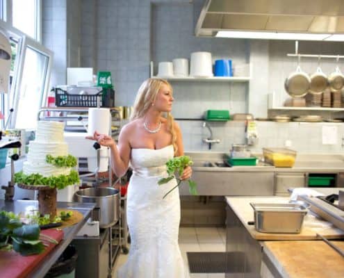 Bride adds green hydrangeas to rustic wedding cake in kitchen at destination wedding at Lake St. Moritz in Switzerland. Gardenias Floral, Waldhaus Hotel.