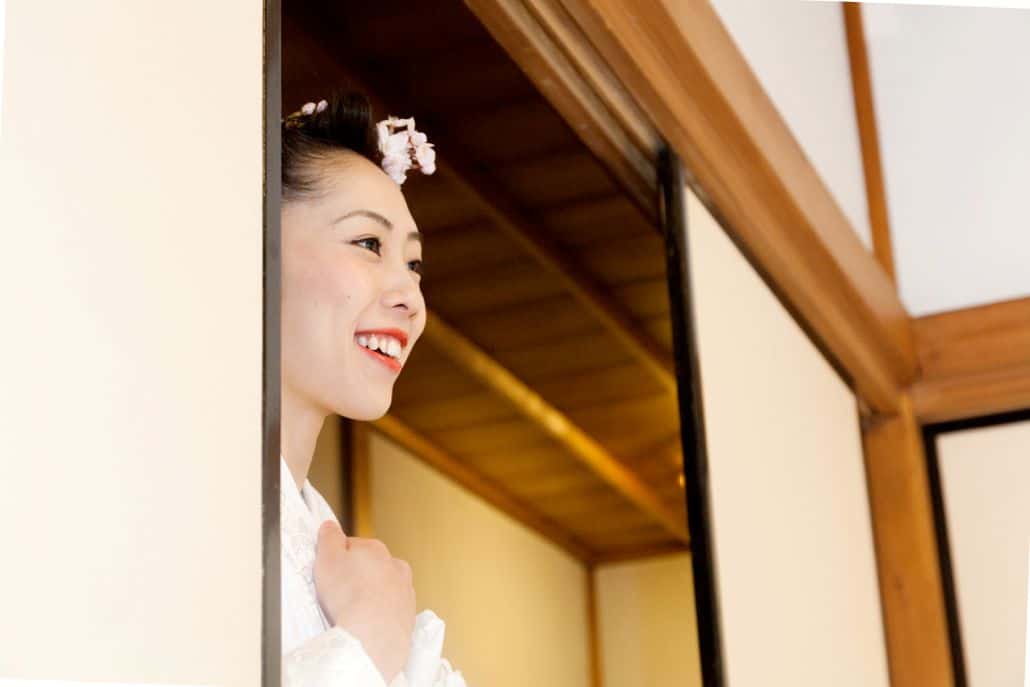Japanese bride smiles at Heian Shrine in Kyoto, white kimono wedding dress, cherry blossoms in bride's hair, Japan destination wedding photographer.