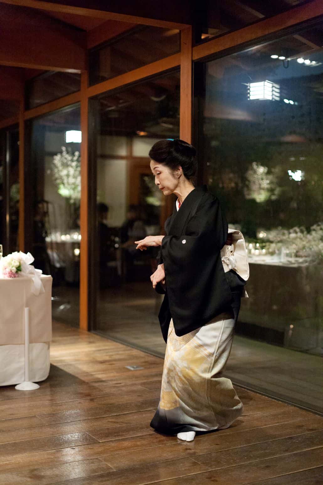 Guest dances in black, ivory and yellow kimono at destination wedding in Kyoto, Japan at Garden Oriental/The Sodoh Higashiyama Kyoto, floor to ceiling windows, destination wedding photography.