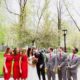 Groom leans head against bride surrounded by wedding party at madison square park wedding photo shoot NYC. red lace bridesmaid dresses from Lulu's, grey groomsmen suits with red ties, David's Bridal wedding dress, red and white wedding bouquet, Spring NYC wedding photos..