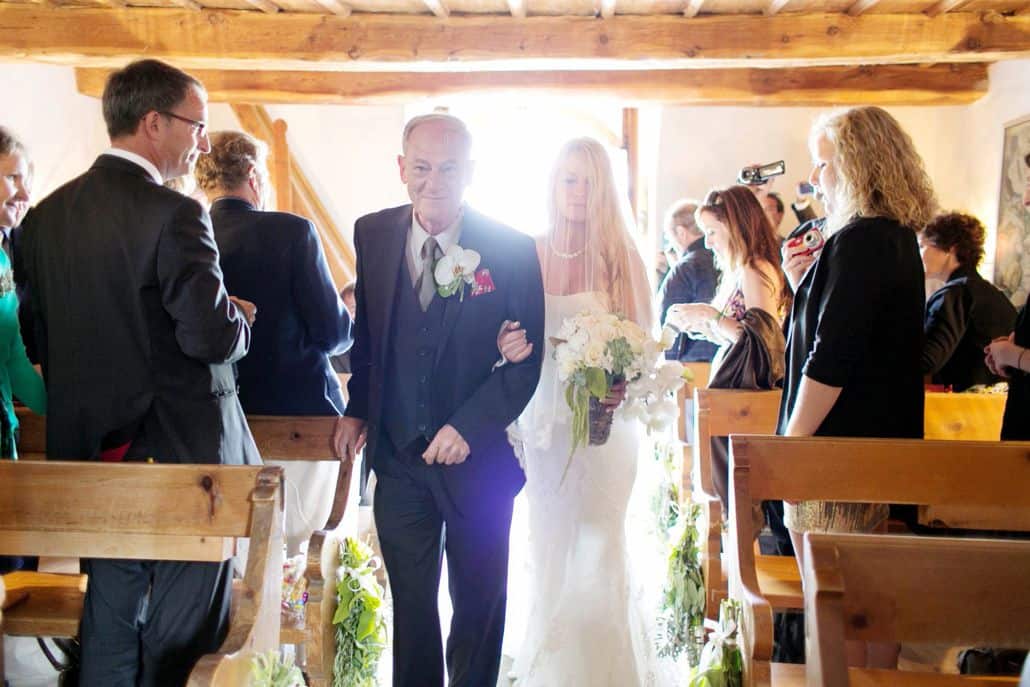 Bride walks down aisle with her father at tiny Romanesque church in the Swiss Alps. European destination wedding photographer, Swiss Alps. Gardenias Floral.