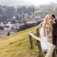 Bride and groom kiss next to old wooden fence on winding dirt path overlooking village in mountains, European destination wedding photography, Switzerland.
